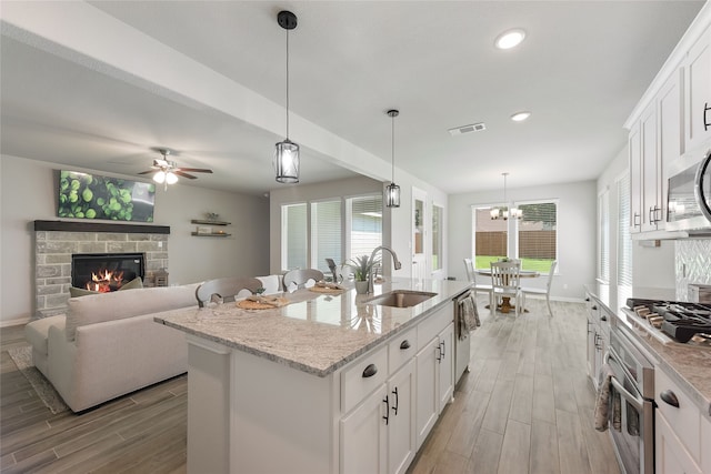 1420 Whitetail Ln, Azle, TX 76020 - kitchen with light wood finished floors, appliances with stainless steel finishes, white cabinets, a kitchen island with sink, and light stone countertops