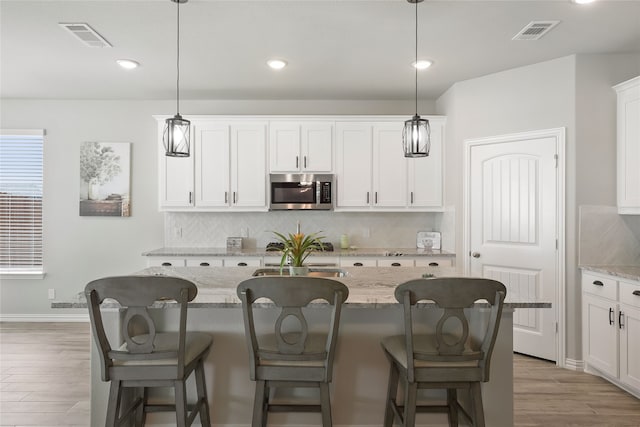 1420 Whitetail Ln, Azle, TX 76020 - kitchen featuring stainless steel microwave, backsplash, light wood-style flooring, white cabinets, and recessed lighting