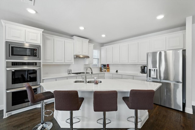 4336 Westminster Ave, Celina, TX 76227 - kitchen with stainless steel appliances, an island with sink, white cabinetry, under cabinet range hood, and a breakfast bar