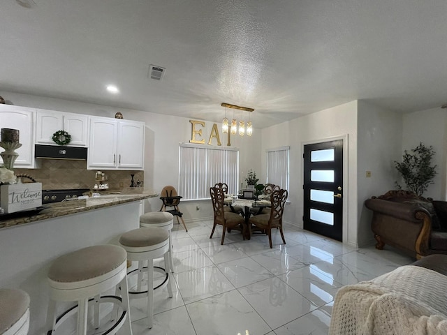 1603 Pacific Ave, Ennis, TX 75119 - kitchen featuring a chandelier, white cabinetry, light marble finish floors, under cabinet range hood, and decorative backsplash