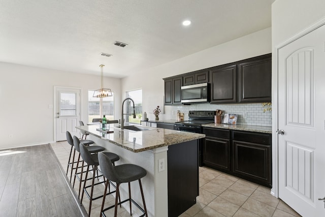 313 Pimlico Way, Ponder, TX 76259 - kitchen with stainless steel microwave, electric range, a kitchen island with sink, decorative backsplash, and a kitchen breakfast bar