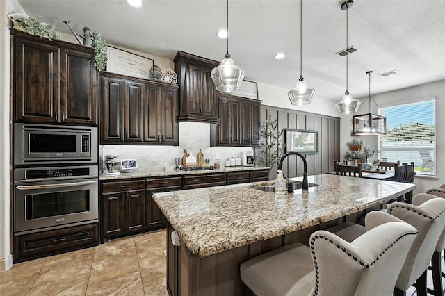 6513 Deer Horn Dr, Fort Worth, TX 76179 - kitchen featuring appliances with stainless steel finishes, a breakfast bar area, decorative backsplash, light stone counters, and pendant lighting