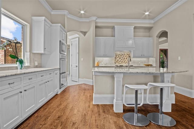 6901 Hickory Hill Cir, Argyle, TX 76226 - kitchen with arched walkways, a kitchen bar, decorative backsplash, white cabinetry, and crown molding