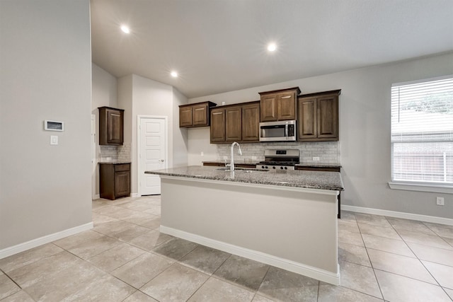 601 Redding Dr, Saginaw, TX 76131 - kitchen with appliances with stainless steel finishes, decorative backsplash, light stone counters, a center island with sink, and lofted ceiling