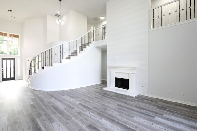 3620 Flintstone Dr, Plano, TX 75074 - unfurnished living room featuring a towering ceiling, stairway, wood finished floors, a fireplace with raised hearth, and a chandelier