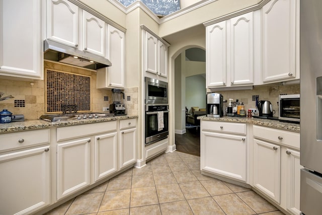 700 Paradise Cv, Shady Shores, TX 76208 - kitchen featuring appliances with stainless steel finishes, under cabinet range hood, decorative backsplash, arched walkways, and light tile patterned flooring