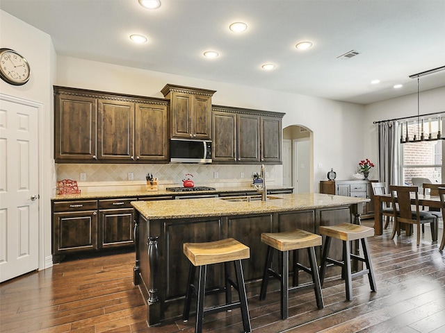505 Peterhouse Dr, Mckinney, TX 75071 - kitchen featuring appliances with stainless steel finishes, arched walkways, dark wood-type flooring, a kitchen bar, and decorative backsplash