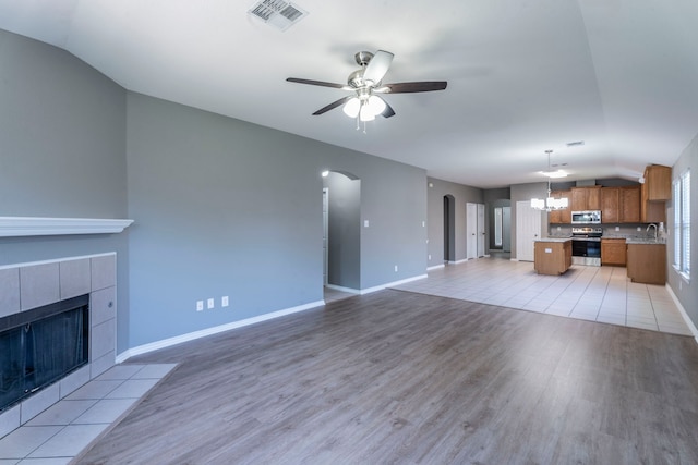 3106 Connor Ln, Wylie, TX 75098 - unfurnished living room with lofted ceiling, arched walkways, ceiling fan, light wood-type flooring, and a tile fireplace