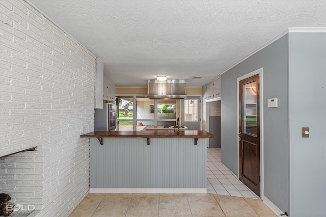 858 River Rd, Shreveport, LA 71105 - kitchen with a breakfast bar area, a peninsula, butcher block countertops, light tile patterned flooring, and ornamental molding