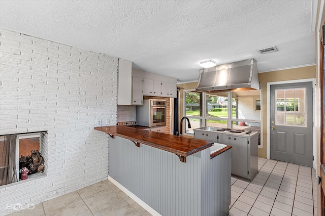 858 River Rd, Shreveport, LA 71105 - kitchen with exhaust hood, stainless steel oven, light tile patterned flooring, a peninsula, and a breakfast bar area