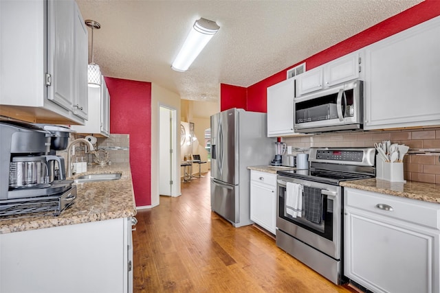 7909 Quest Ct, Frisco, TX 75035 - kitchen with stainless steel appliances, light wood finished floors, decorative backsplash, white cabinetry, and a textured ceiling