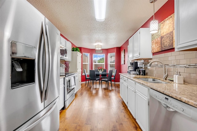 7909 Quest Ct, Frisco, TX 75035 - kitchen featuring appliances with stainless steel finishes, a textured ceiling, white cabinets, light wood-type flooring, and backsplash