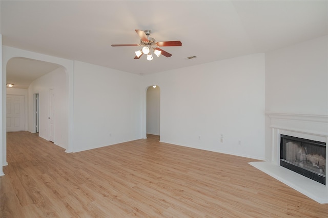 2912 Lighthouse Dr, Denton, TX 76210 - unfurnished living room featuring arched walkways, ceiling fan, light wood-style floors, and a fireplace with raised hearth