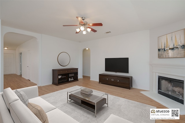 2912 Lighthouse Dr, Denton, TX 76210 - living area with arched walkways, a ceiling fan, light wood-style floors, and a fireplace with raised hearth