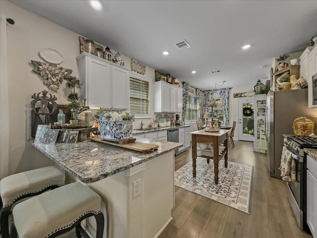 2332 Evening Stone Dr, Little Elm, TX 76227 - kitchen with appliances with stainless steel finishes, a peninsula, light stone countertops, wood finished floors, and recessed lighting