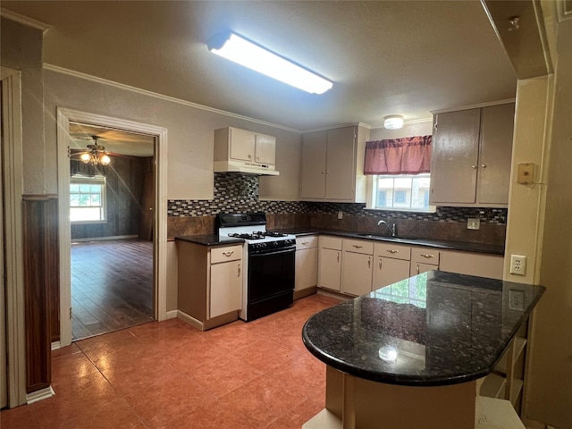 717 N 37th St, Corsicana, TX 75110 - kitchen featuring black gas stove, under cabinet range hood, backsplash, a peninsula, and crown molding