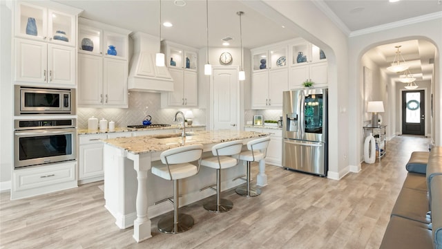 2809 Burgundy Trl, Rowlett, TX 75088 - kitchen featuring stainless steel appliances, premium range hood, arched walkways, light wood-style floors, and ornamental molding