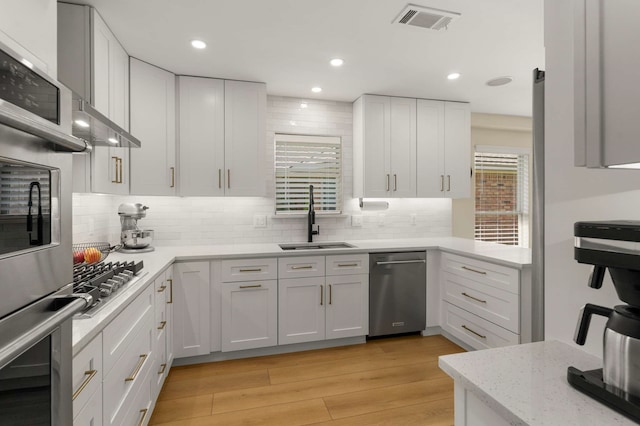 6207 Crested Butte Dr, Dallas, TX 75252 - kitchen featuring stainless steel appliances, decorative backsplash, white cabinetry, light wood finished floors, and light stone counters