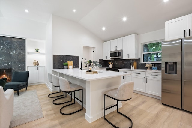 2605 S Glenbrook Dr, Garland, TX 75041 - kitchen with appliances with stainless steel finishes, a kitchen breakfast bar, light wood-type flooring, white cabinets, and vaulted ceiling