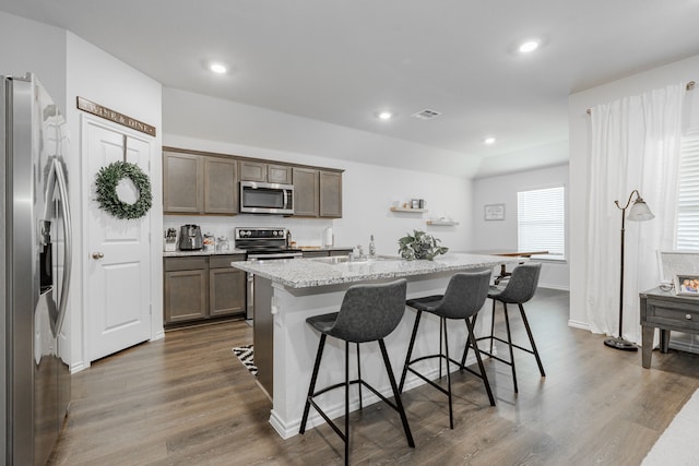 3216 Everly Dr, Fate, TX 75189 - kitchen featuring appliances with stainless steel finishes, dark wood-type flooring, a kitchen bar, a center island with sink, and light stone counters