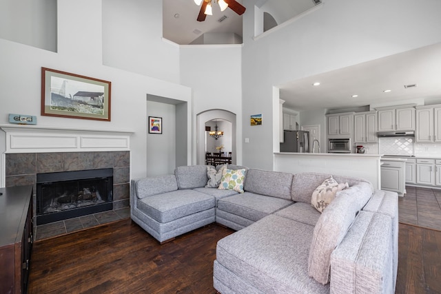 3912 Appleton Ln, Flower Mound, TX 75022 - living room featuring ceiling fan, dark wood-style flooring, arched walkways, a fireplace, and a towering ceiling