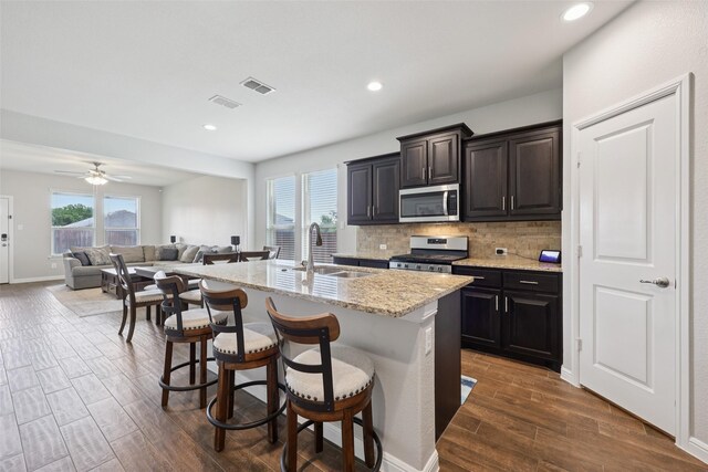 1083 Admiral Dr, Azle, TX 76020 - kitchen featuring appliances with stainless steel finishes, a kitchen island with sink, dark wood-style flooring, decorative backsplash, and a kitchen breakfast bar
