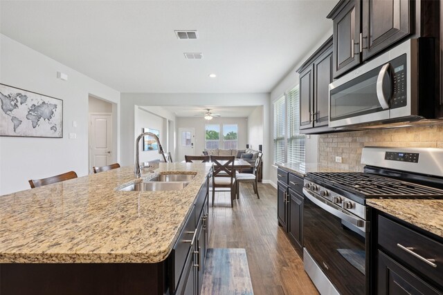 1083 Admiral Dr, Azle, TX 76020 - kitchen featuring appliances with stainless steel finishes, dark wood-style floors, an island with sink, tasteful backsplash, and light stone countertops