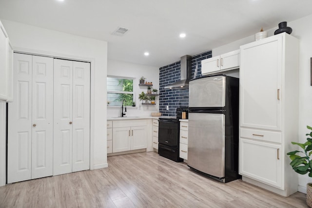 3005 Pate Dr, Fort Worth, TX 76105 - kitchen with freestanding refrigerator, black / electric stove, wall chimney exhaust hood, white cabinetry, and light wood-style flooring