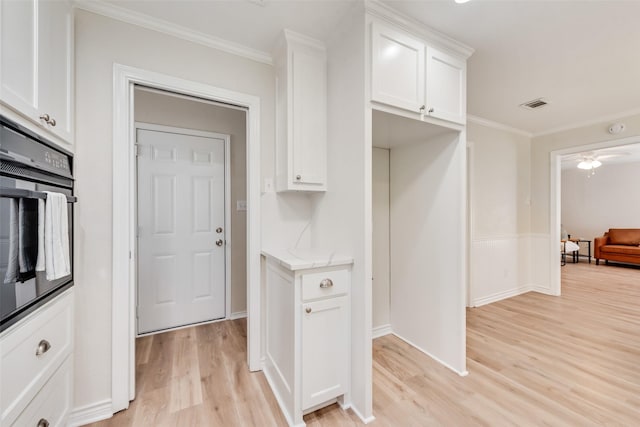 5504 Whitman Ave, Fort Worth, TX 76133 - kitchen with black oven, light wood-style floors, white cabinets, ornamental molding, and light stone counters