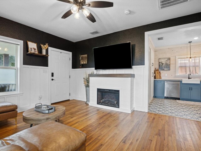 309 E 3rd St, Maypearl, TX 76064 - living room featuring light wood-style flooring, ceiling fan, a wainscoted wall, and a fireplace