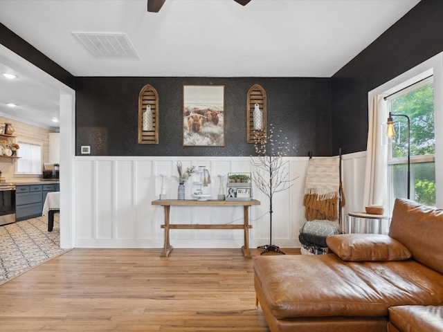 309 E 3rd St, Maypearl, TX 76064 - sitting room featuring ceiling fan, healthy amount of natural light, wainscoting, light wood-type flooring, and a decorative wall
