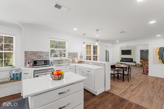 107 Preston Ave, Shreveport, LA 71105 - kitchen featuring appliances with stainless steel finishes, a peninsula, dark wood finished floors, white cabinets, and a glass covered fireplace