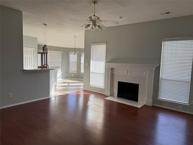 1401 Williams Crk, Mesquite, TX 75181 - unfurnished living room featuring ceiling fan, a textured ceiling, wood finished floors, a tiled fireplace, and a chandelier