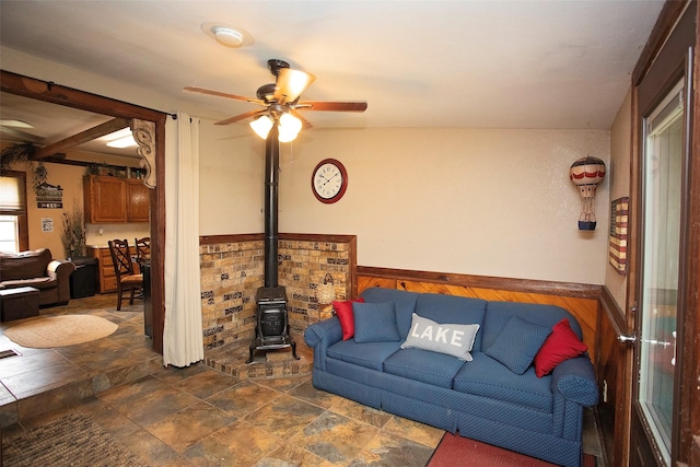 10234 County Road 198, Breckenridge, TX 76424 - living room featuring ceiling fan, a wood stove, a wainscoted wall, dark stone finish flooring, and wooden walls