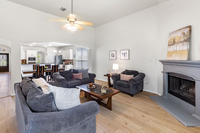 584 Indian Hill Dr, Oak Point, TX 75068 - living room featuring arched walkways, a fireplace with raised hearth, light wood finished floors, a towering ceiling, and a ceiling fan