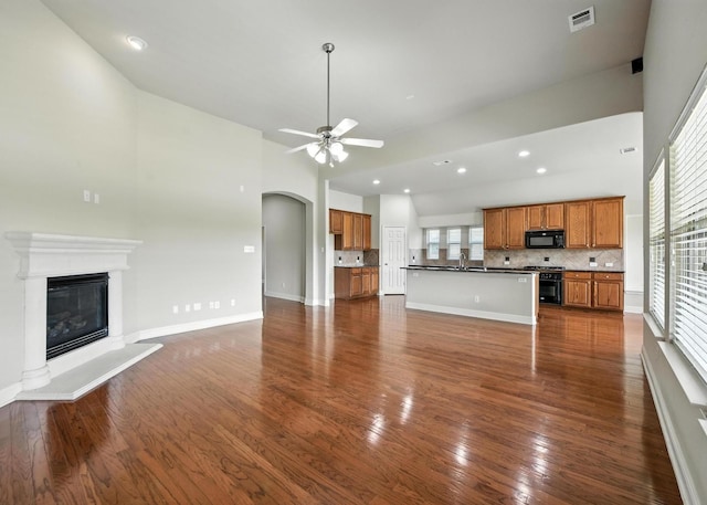 8120 Tyler Dr, Lantana, TX 76226 - unfurnished living room featuring a ceiling fan, high vaulted ceiling, dark wood-style flooring, a glass covered fireplace, and arched walkways