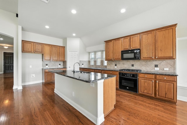 8120 Tyler Dr, Lantana, TX 76226 - kitchen featuring black appliances, brown cabinetry, dark wood finished floors, dark stone countertops, and a kitchen island with sink