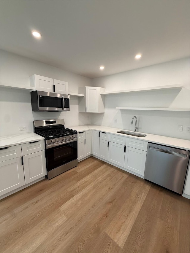 1019 E Waco Ave, Dallas, TX 75216 - kitchen featuring appliances with stainless steel finishes, open shelves, white cabinets, light wood-type flooring, and light countertops
