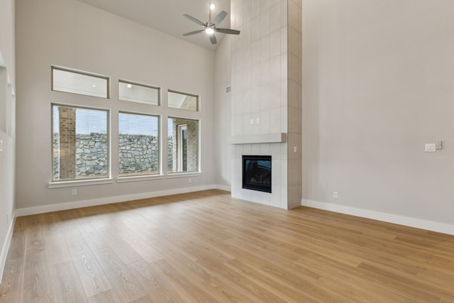 4505 N Summit View Dr, Mckinney, TX 75071 - unfurnished living room with light wood-type flooring, a ceiling fan, a tile fireplace, and a towering ceiling