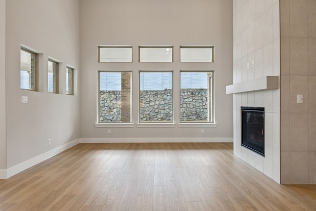 4505 N Summit View Dr, Mckinney, TX 75071 - unfurnished living room with light wood-style flooring, a tile fireplace, and a towering ceiling