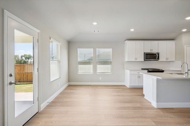 117 Whitlow Dr, Princeton, TX 75071 - kitchen featuring stainless steel microwave, light wood-style floors, white cabinets, light countertops, and tasteful backsplash