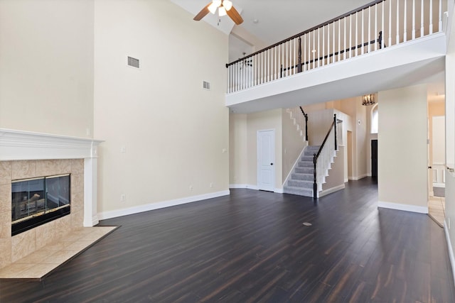 8516 Ontario Dr, Mckinney, TX 75072 - unfurnished living room featuring a towering ceiling, stairs, ceiling fan, dark wood-style flooring, and a tiled fireplace