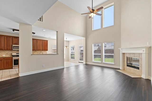 8516 Ontario Dr, Mckinney, TX 75072 - unfurnished living room featuring wood finished floors, ceiling fan, a fireplace, a towering ceiling, and a chandelier