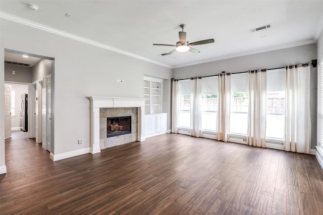 2400 Silverstone Ln, Mckinney, TX 75072 - unfurnished living room featuring a ceiling fan, crown molding, dark wood-type flooring, a fireplace, and built in shelves