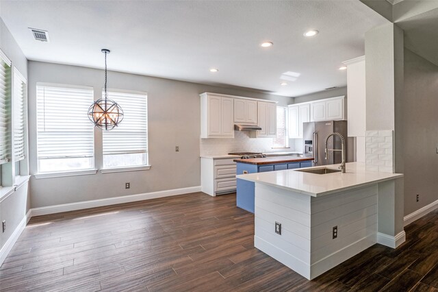 2400 Silverstone Ln, Mckinney, TX 75072 - kitchen with under cabinet range hood, dark wood-style floors, decorative backsplash, white cabinets, and a peninsula