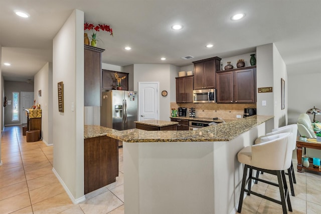 520 Rustic Oak Ln, Mckinney, TX 75072 - kitchen with appliances with stainless steel finishes, light tile patterned flooring, light stone counters, dark brown cabinets, and decorative backsplash