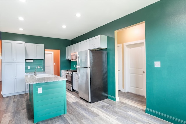 392 Calle Cedro Dr, Sherman, TX 75090 - kitchen with stainless steel appliances, light wood finished floors, light stone countertops, an island with sink, and white cabinetry