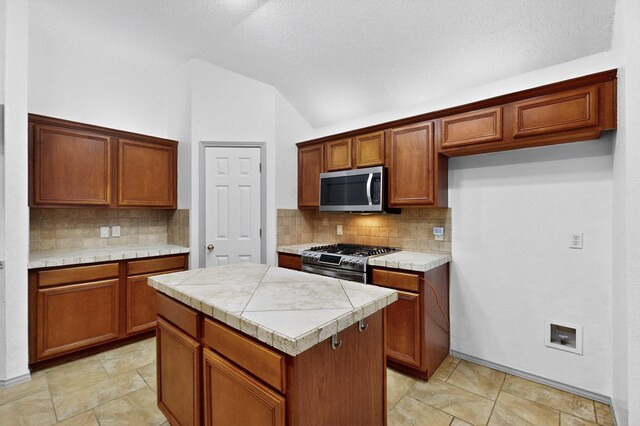 201 Settlers Glen Trl, Arlington, TX 76002 - kitchen featuring appliances with stainless steel finishes, a kitchen island, vaulted ceiling, decorative backsplash, and brown cabinets