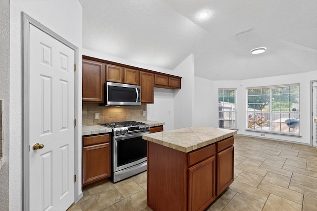 201 Settlers Glen Trl, Arlington, TX 76002 - kitchen with appliances with stainless steel finishes, vaulted ceiling, decorative backsplash, brown cabinets, and a kitchen island