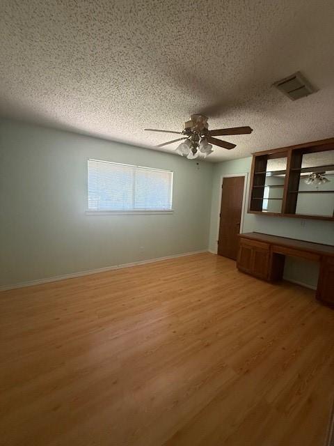 8761 S County Rd, Frisco, TX 75034 - unfurnished bedroom featuring a textured ceiling, built in desk, light wood-style floors, and ceiling fan